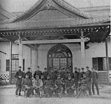 Photographie de groupe d'officiers en uniforme devant un bâtiment japonais à large toiture et porche sculpté