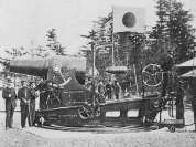 Photographie ancienne d'une pièce d'artillerie de gros calibre sur affût tournant, servants et drapeau japonais