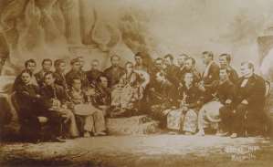 Document d'archive reproduit dans le recueil Photographie de groupe ancienne en studio, Occidentaux en costume et Japonais en kimono devant une toile peinte